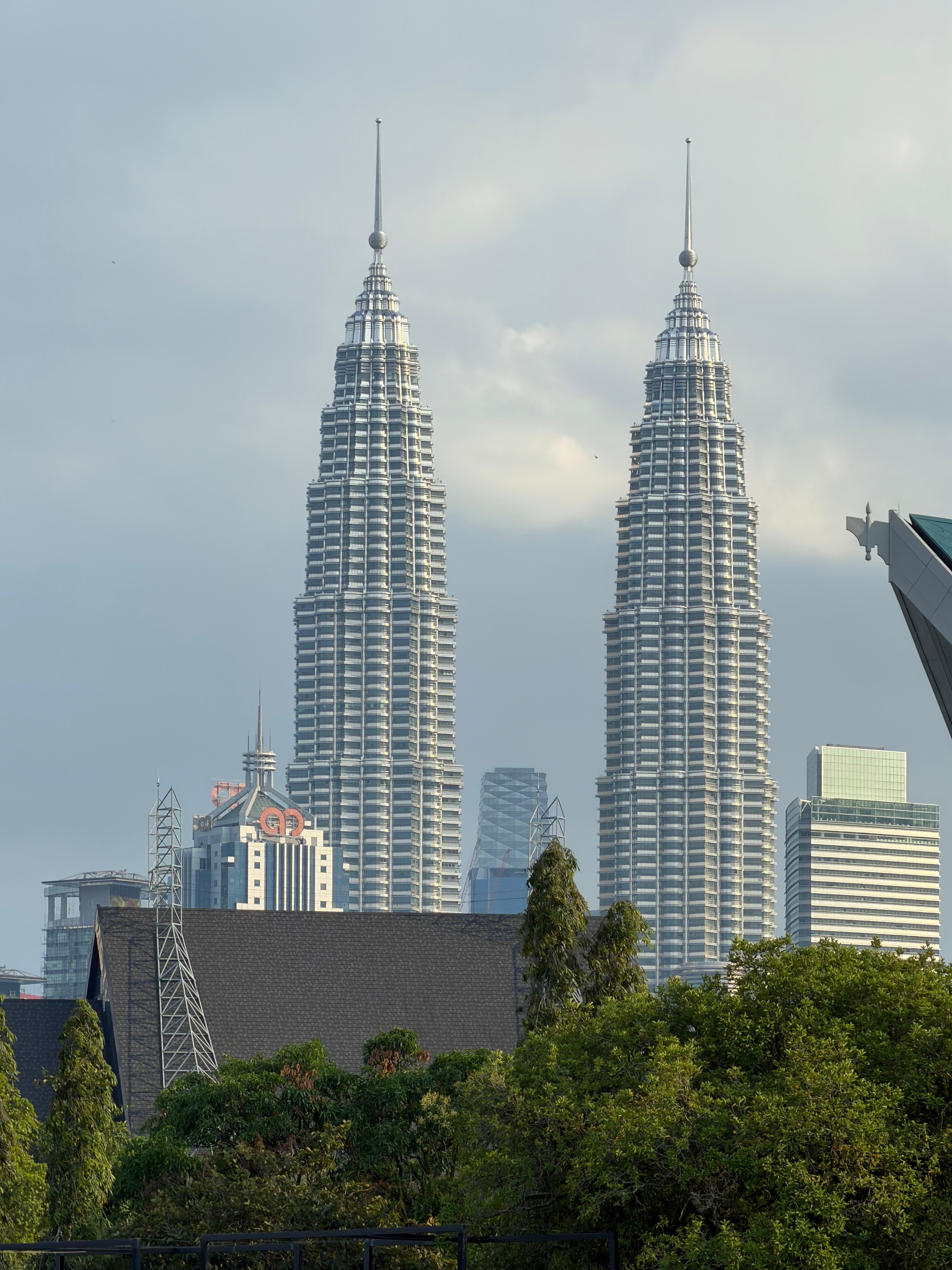 The Petronas Towers of Kuala Lumpur are seen in the distance from Titiwangsa park. The twin towers are overlooking the city against a blue sky with white clouds